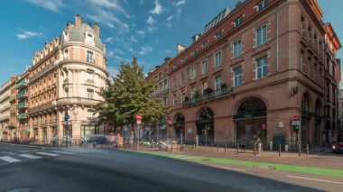 Toulouse, Occitanie, Fransa 'da Rue de Metz' in zaman çizelgesini gösteren panorama, tarihi cepheleri, dükkanları, kafeleri, trafiği ve mavi bulutlu gökyüzünü gösteriyor. Şehrin göbeğinde canlı bir şehir manzarası