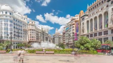 Valencia, İspanya 'da Belediye Meydanı Plaza del Ayuntamiento zaman atlaması hipervane. Büyük mimari, çiçek açan yeşillik ve bulutlu bir gökyüzünün altında su jetleri. İnsanlar canlı meydanda geziniyor..
