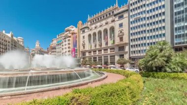 Panorama, Valencia, İspanya 'da Belediye Meydanı Plaza del Ayuntamiento zaman kapsülünü gösteriyor. Büyük mimari, çiçek açan yeşillik ve mavi gökyüzünün altında su jetleri. İnsanlar meydanda geziniyor.