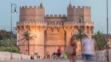 Serrans Kuleleri Torres de Serranos günden geceye Valencia, İspanya 'daki geçiş zamanı. Şehrin antik duvarlarından gelen büyük bir ortaçağ kapısı. İnsanlar tarihi bir dönüm noktasının yakınındaki bir köprüde yürüyorlar.