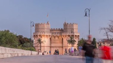 Serrans Kuleleri Torres de Serranos günden geceye Valencia, İspanya 'daki geçiş zamanı. Şehrin antik duvarlarından gelen büyük bir ortaçağ kapısı. İnsanlar tarihi bir yere yakın bir köprüde yürüyorlar.
