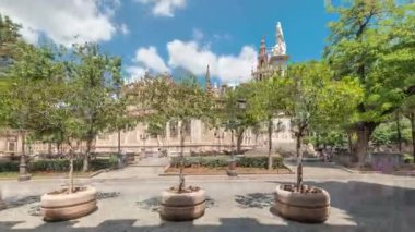 Plaza del Triunfo zaman atlaması ve Sevilla Katedrali 'nin kusursuz gebelik anıtı. Yeşil ağaçlar, tarihi mimari, bulutlu mavi gökyüzü. Endülüs, İspanya 'da manzara