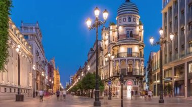 Avenida de la Constitucion, Seville, İspanya 'da günden geceye zaman dilimi. Iconic Adriatica binası gün batımından sonra parlıyor. Modern sokak lambaları, yayalar ve şehir atmosferine sahip tarihi mimari