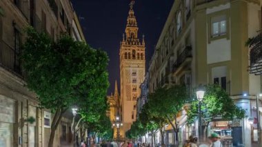 Barrio Santa Cruz 'un Seville, İspanya' daki gece zamanı. Arka planda Giralda kulesi aydınlanıyor. Turistler ve yerliler kafeler ve dükkanlarla dolu büyüleyici kaldırım taşları caddelerinde yürüyorlar..
