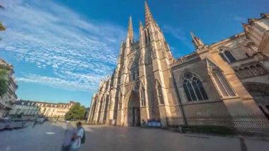 Saint-Andre de Bordeaux Katedrali, mavi bulutlu gökyüzünün altında ikiz kuleleri olan hızlandırılmış zaman atlaması. Meydanda yürüyen insanlar gün batımından önce sakin bir şehir atmosferi yaratıyorlar. Bordeaux, Fransa