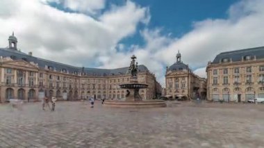 Place de la Bourse zaman atlaması Fransa 'nın Bordeaux şehrinde, Bulutlu mavi gökyüzünün altında klasik mimari ile çevrili Üç Zarafet Çeşmesi ile birlikte. Meydanda yürüyen insanlar.