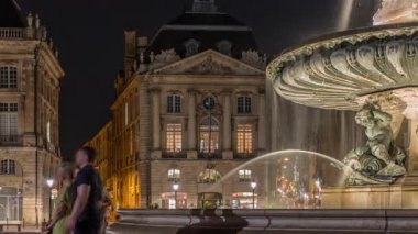 Place de la Bourse manzarası ve Fransa 'nın Bordeaux şehrindeki çeşme zamanı. Aydınlatılmış tarihi binalar büyük meydanın sınırında. Lokantada parlayan pencereler