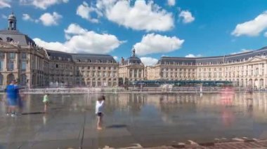 Place de la Bourse ve Miroir deau hiperlapse Bordeaux, Fransa 'da, tarihi mimariyi yansıtıyor. Turistler şehir simgesi ve çeşmenin tadını çıkarıyorlar. Trafik ve tramvay zamanı geçiyor..