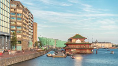 Sudaki pagoda şeklinde bir Çin restoranının hipervanesi, tarihi şehir merkezi binalarının ve günbatımında modern mimarinin arka planına karşı kurulur. Amsterdam, Hollanda