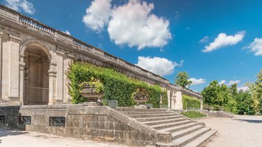 Fransa 'nın başkenti Jardin' de Palais du Capitole 'de zaman atlaması. Sarmaşık kaplı yeşil ağaçlar, merdivenler ve parlak mavi bulutlu gökyüzü ile çevrili tarihi bir binanın manzarası.