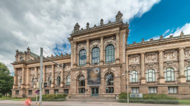 Hanover 'in Aşağı Saksonya Devlet Müzesi' nin trafik ve tarihi ön cephelerinin önünden geçen insanlar. Bulutlu gökyüzü, Almanya 'nın Niedersachsen zaman diliminde kültürel dönüm noktasını çerçeveledi