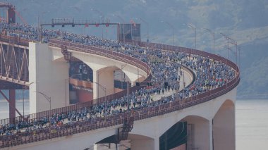 Lizbon 'da koşmak 25 Nisan köprüsünü yukarıdan Tagus nehri hava manzarası üzerinden geçmek demek. Yolun kıvrımlı kısmında baştan sona büyük bir kalabalık köprüden aşağı ilerliyor.