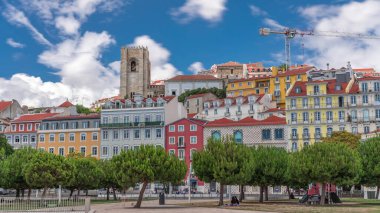 Kare largo Jose Saramago zaman atlaması Lizbon 'da ortaçağ Alfama' sında, güneşli bir günde yeşil ağaçlar ve mavi bulutlu gökyüzü. Birçok renkli ev ve tepesinde Se de Lisboa katedrali var. Portekiz
