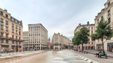 Fransa 'nın Lyon şehrindeki Place de la Republique' in hiperlapesi. Meydanda, tarihi binalarla çevrili büyük bir çeşme var ve insanlar banklarda oturuyor.