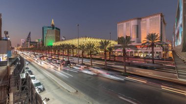 Suudi Arabistan, Riyad 'daki Kral Fahd Yolu' nun hava-gece zaman çizelgesi. Modern kuleler ve gökdelenlerle çevrili aydınlık Ulusal Kütüphane 'nin yakınındaki arabalarla ve taksilerle hareketli bir trafik manzarası.