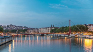 Lyon 'daki Saone Nehri' nin üzerindeki Palais du Justice Köprüsü 'nde, günden geceye geçiş. Rıhtımdaki aydınlık binalar gün batımından sonra suya yansıyor.