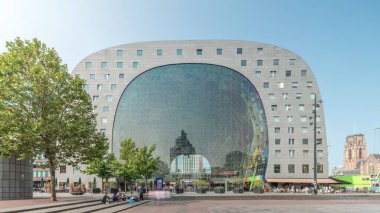 Rotterdamse Markthal 'ın dış yüzeyinde aşırı kayma. Dükkanları ve restoranları olan ikonik at nalı şeklinde bir bina. Meydanda gezinen insanlar. Gökdelenler ve arka planda canlı bir şehir manzarası