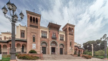 Maria Luisa Park 'taki Sevilla Sanat ve Gelenekler Müzesi cephesi. Plaza de America 'da Mudejar tarzı bir bina var. Bulutlu gökyüzü altında zaman atlaması. Sevilla, İspanya.
