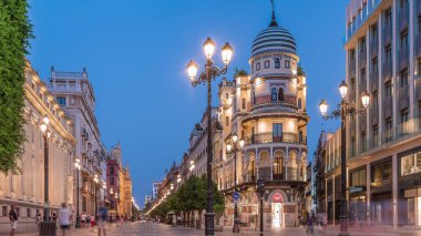 Avenida de la Constitucion, Seville, İspanya 'da günden geceye zaman dilimi. Iconic Adriatica binası gün batımından sonra parlıyor. Modern sokak lambaları, yayalar ve şehir atmosferine sahip tarihi mimari