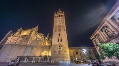 La Giralda ve Seville Katedrali geceleri aşırı hızlanarak altın ışıklarla parıldıyor. Tarihi çan kulesi, gotik detaylar ve aydınlatılmış sokaklar Sevilla, İspanya 'da büyülü bir atmosfer yaratıyor.