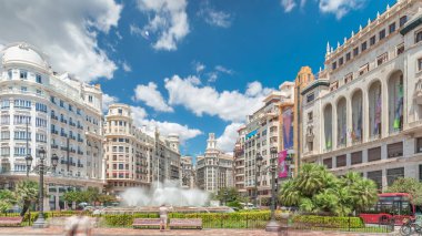 Valencia, İspanya 'da Belediye Meydanı' ndaki (Plaza del Ayuntamiento Meydanı) zaman atlaması. Büyük mimari, çiçek açan yeşillik ve bulutlu bir gökyüzünün altında su jetleri. İnsanlar canlı meydanda geziniyor..