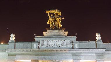 Sculpture Tractor operator and collective farmer on the top of entrance to All-Russia Exhibition Centre timelapse hyperlapse. Moscow, Russia. Orange illumination at night