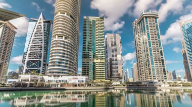 Rıhtımdaki gökdelenlerin hiperlapse görüntüsü. Jumeirah Gölü Kuleleri 'ndeki yerleşim yerleri Dubai, BAE' deki su saatlerine göre yansıdı. Rıhtımdan mavi bulutlu gökyüzü