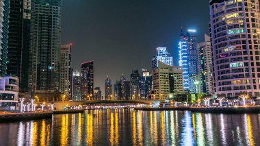 Dubai Marina gezinti güvertesinde yatlar ve modern kuleler Dubai 'deki deniz kıyısından yansıyan su, Birleşik Arap Emirlikleri. Köprü ve gökdelenler