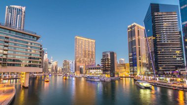 Dubai Marina rıhtımında yatları ve alışveriş merkezi yakınlarındaki modern kuleleri olan Dubai 'de güneş battıktan sonraki gece, Birleşik Arap Emirlikleri. Dubai Marina, Dubai 'de bir şehirdir.