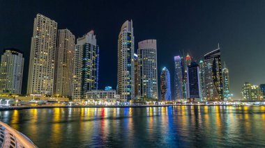 Dubai Marina gezinti güvertesinde yatlar ve modern kuleler Dubai 'deki deniz kıyısından yansıyan su, Birleşik Arap Emirlikleri' nin gece hiperhızlandırması. Yapay kanalla aydınlatılmış bölge