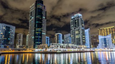Dubai Marina kanalı üzerinde tekne ve köprüler bulunan, Dubai 'deki deniz kıyısından suya yansıyan palmiyeler ve modern kuleler, Birleşik Arap Emirlikleri' nin gece vakti aşırı hızlanması. Aydınlatılmış gökdelenler