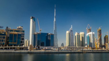 Dubai 'nin iş sahasının ufuk çizgisi gündüz gökdelenleri ile birlikte mavi gökyüzü ve suya yansıyan hiperhızlandırılmış. Şehir merkezinde arka planda.
