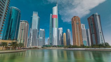 Rıhtımdaki palmiyeli gökdelenlerin hızlandırılmış görüntüsü. Jumeirah Lake Towers semtinde camla kaplı konut binaları Dubai, BAE 'de suya yansıdı. Rıhtımdan görüntüle