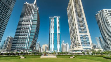 Rıhtımdaki palmiyeli gökdelenlerin hızlandırılmış görüntüsü. Dubai, BAE 'deki parkın yakınındaki Jumeirah Gölü Kuleleri' nde camla kaplı konut binaları. Parktan görüntüle