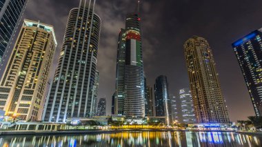 Rıhtımdaki ışıklandırılmış gökdelenlerin gece görüş açısını hızlandırın. Dubai, BAE 'deki Jumeirah Gölü Kuleleri' ndeki konut binaları. Rıhtımdan görüntüle