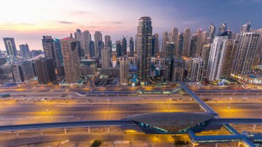 Dubai Marina ve Dubai, BAE 'deki JLT gökdelenlerinin hava üzerinden gece gündüz geçiş zamanı. Modern kuleler ve Şeyh zayed yolundaki trafik yukarıdan metro ve tramvay istasyonlarıyla