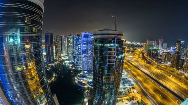 Dubai Marina ve Dubai, BAE 'deki JLT gökdelenlerinin gece görüntüsü. Yanıp sönen ışıkları, gölü ve yolda metro hattı ve tramvay istasyonuyla aydınlanan modern kuleler.