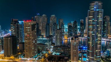 Dubai Marina gezinti güvertesi ve kanalı, Dubai, BAE 'de yüzen yat ve teknelerle dolu. Yanıp sönen ışıkları ve yol trafiği olan aydınlık modern kuleler.
