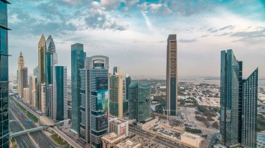 Dubai downtown skyline timelapse at sunset with financial center skyscrapers and Sheikh Zayed road traffic. Top aerial view from tower rooftop. Clouds on the sky. Dubai, United Arab Emirates