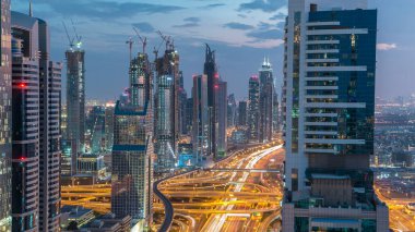 Dubai şehir mimarisi günden geceye geçiş zamanı. Şeyh Zayed yolu üzerindeki gökdelenler aydınlanmış ve kavşakta trafik var. Güzel bulutlu gökyüzü