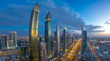 Dubai şehir mimarisi günden geceye geçiş zamanı. Şeyh Zayed yolu üzerindeki aydınlık gökdelenler ve trafik manzaralı üst hava manzarası. Güzel bulutlu gökyüzü. Fisheye merceği