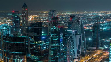 Dubai iş hangarı kuleleri gece vakti aydınlatılıyor. Otoyol trafiği. Bazı gökdelenlerin çatısı ve inşaat halindeki yeni kulelerin havadan görüntüsü.