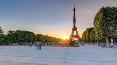Güneş batarken Champ de Mars 'tan görülen Eyfel Kulesi, Paris, Fransa. İnsanlar çimenlerde oturup yürüyorlar. Açık gökyüzü ve güneşli bir yaz akşamı