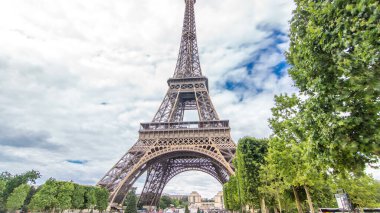 Champ de Mars ve Eyfel Kulesi güneşli bir yaz gününde hızlandırılmış zaman atlaması. Paris, Fransa. Yeşil ağaçlar ve bulutlu gökyüzü. Geri çekiliyorum