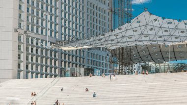 Paris 'teki Savunma Ticaret Bölgesi' ne yakın çekim zamanı. İnsanlar gün boyunca merdivenlerde oturuyor. Paris, Fransa. Yazın mavi bulutlu gökyüzü.