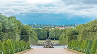 Bahçede bakımlı bir sokak ve yukarıdan gelen zaman aralığında çeşme. Versailles Şatosu 'nda (Chateau de Versailles) güzel bir bahçe, Fransa. Yaz gününde dramatik bulutlu gökyüzü