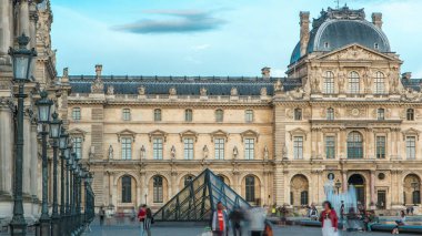 Louvre Harici Binası 'ndaki eski ve yeni elementler. Paris, Fransa. Turistler yaz günü gün batımından önce bulutlu gökyüzüyle meydanda yürürler. Sokak lambaları.