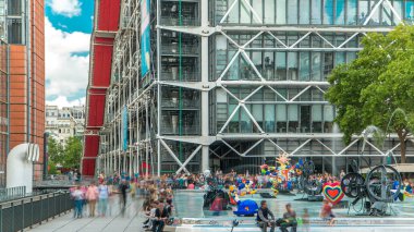 Centre Pompidou 'daki Çeşme, Ulusal Modern Sanat Müzesi. Paris, Fransa. İnsanlar yaz günü parktaki meydanda mavi bulutlu gökyüzüyle dinleniyorlar.