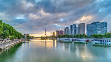 Eyfel Kulesi, Seine Nehri 'nde ve Fransa' nın Paris şehrinde teknelerle gün doğumu zamanı. Mirabeau Köprüsü 'nden gökyüzü dramatik bir şekilde görünüyor. Modern binalar ve yol trafiği. Özgürlük Anıtı