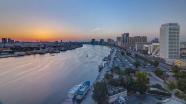 Dubai creek manzara tekneler ve yatlar ile günbatımı timelapse ve trafik yol ve otopark ile modern binalar. Yukarıdan hava üstten görünüm